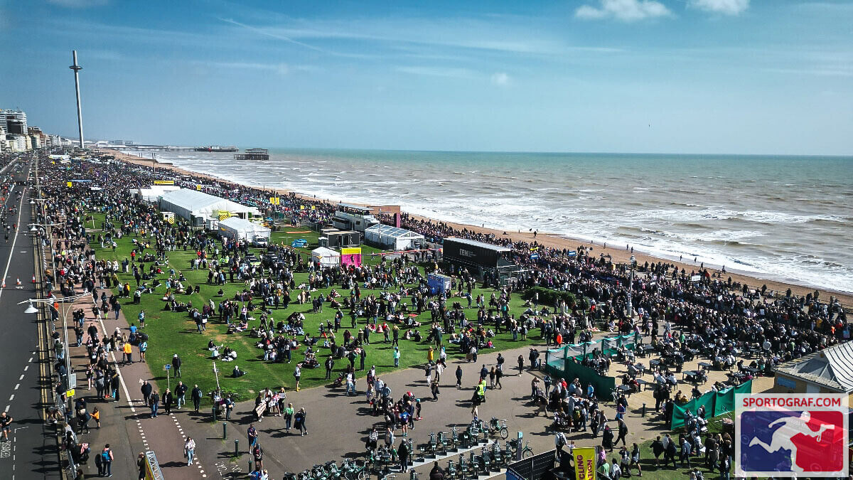 A wide shot of Brighton & Hove beach with the race village and thousands of people in the foreground